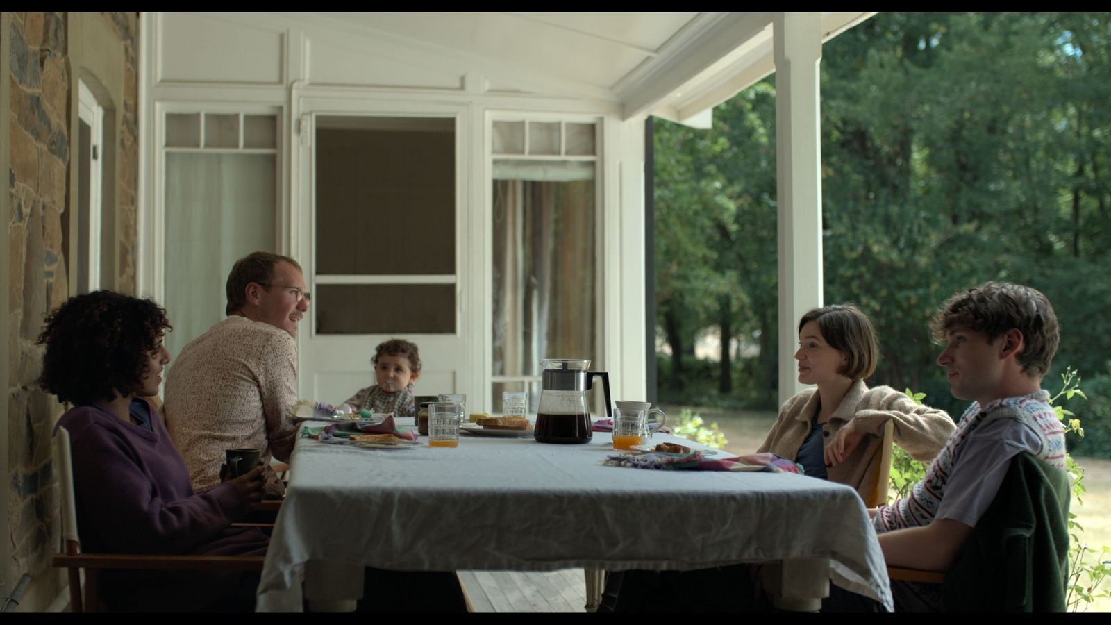 The characters from Alphabet Lane sit at a table on a white veranda, opposite another young couple and their toddler. A coffee pot and orange juice are on the table.