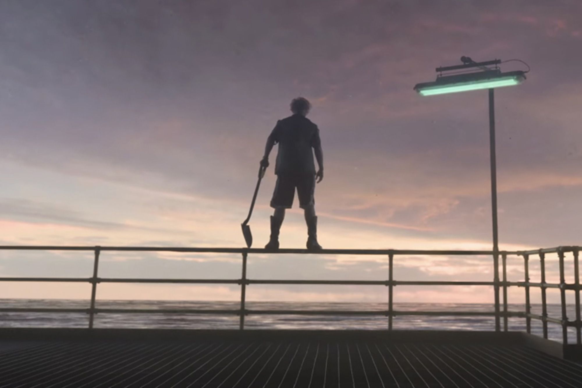 Tom Cruise silhouetted as Digger, holding a shovel standing on a railing overlooking the sea